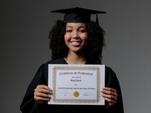 Eine junge Frau hält eine Urkunde. Sie trägt graduierten Kleidung. 