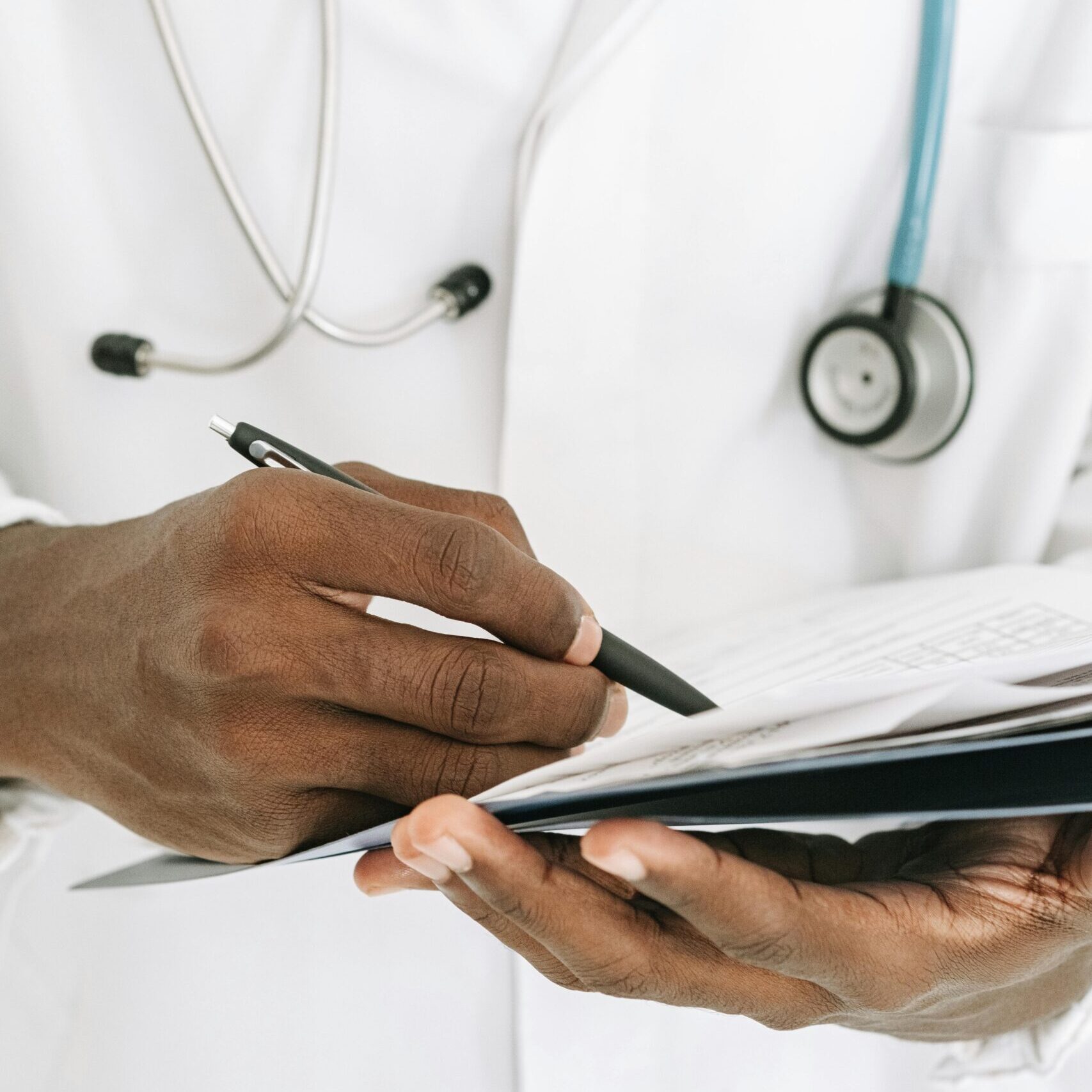 Ein Arzt füllt mit der rechten Hand Dokumente aus, die in seiner linken Hand liegen.