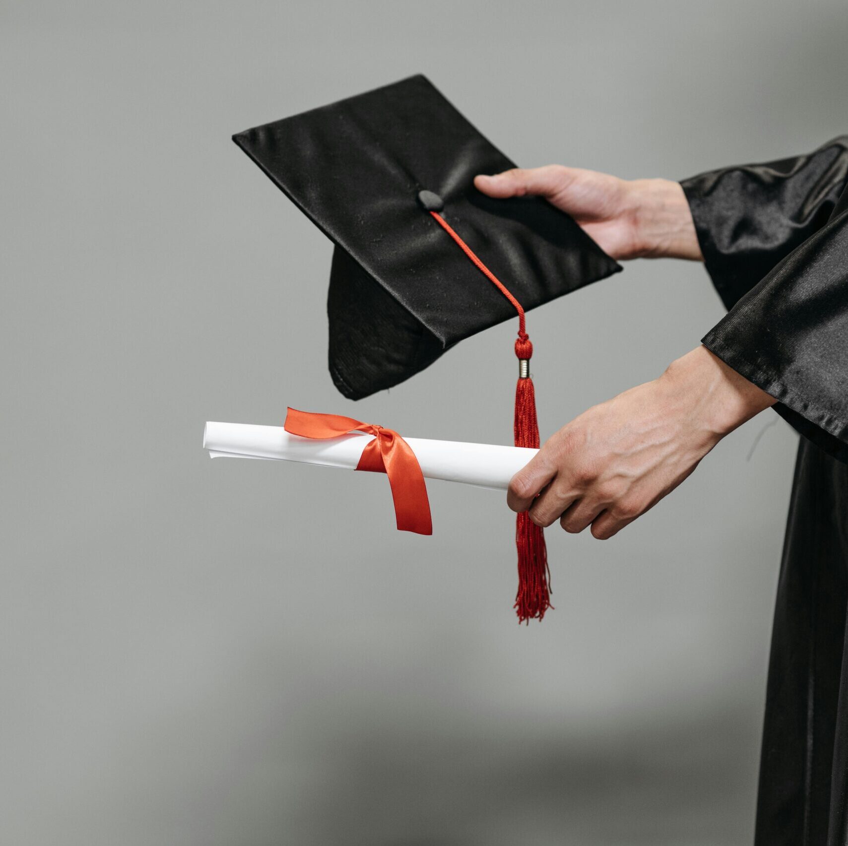 Es werden eine graduierten Mütze und ein eingerolltes Zeugnis in das Bild gehalten. 